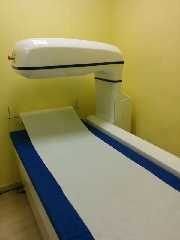 In una stanza gialla, un lettino per la TAC ospedaliera con imbottitura blu sotto un dispositivo di diagnostica per immagini bianco.
