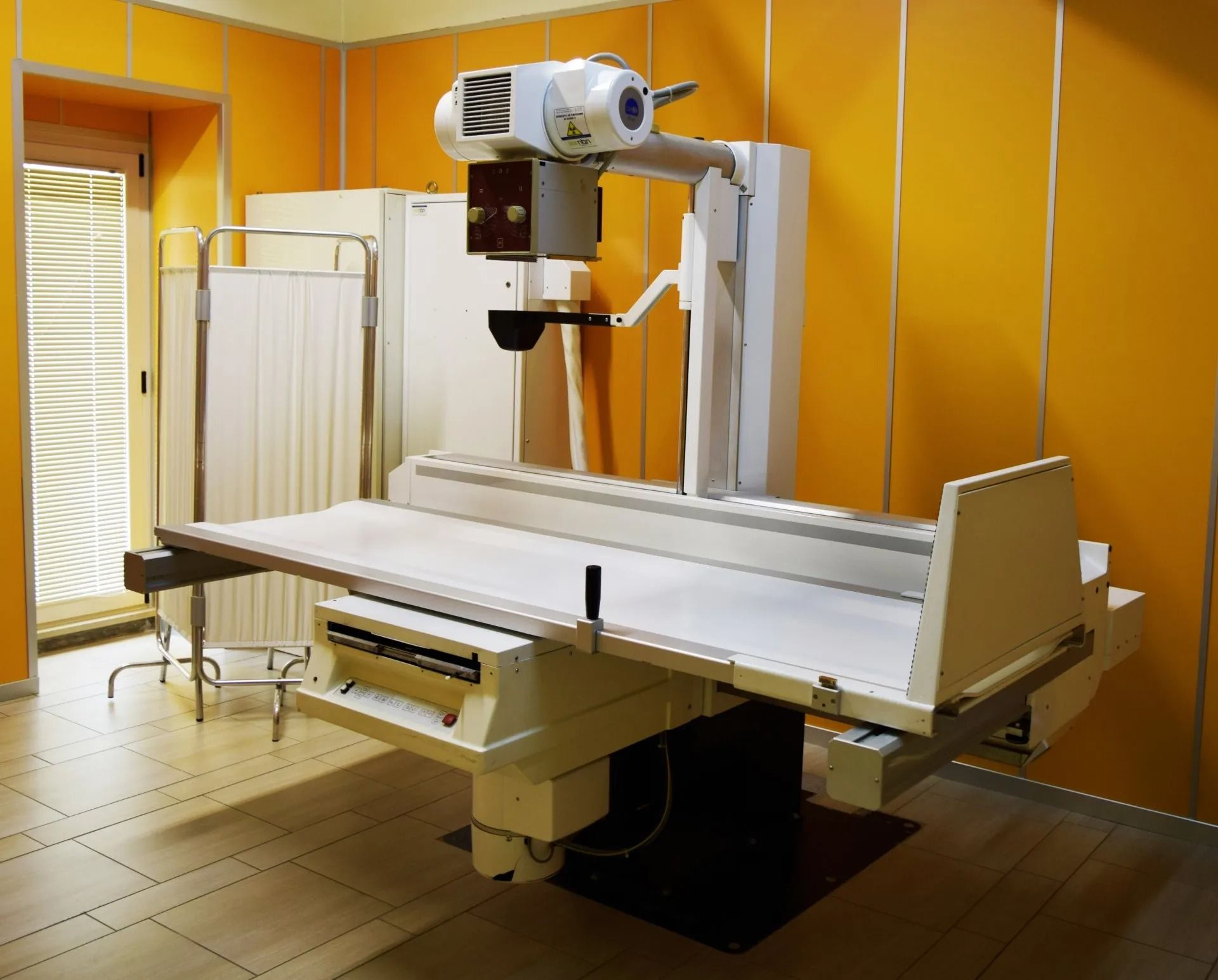 Apparecchio radiografico medico in una stanza con pareti arancioni e pavimento piastrellato.