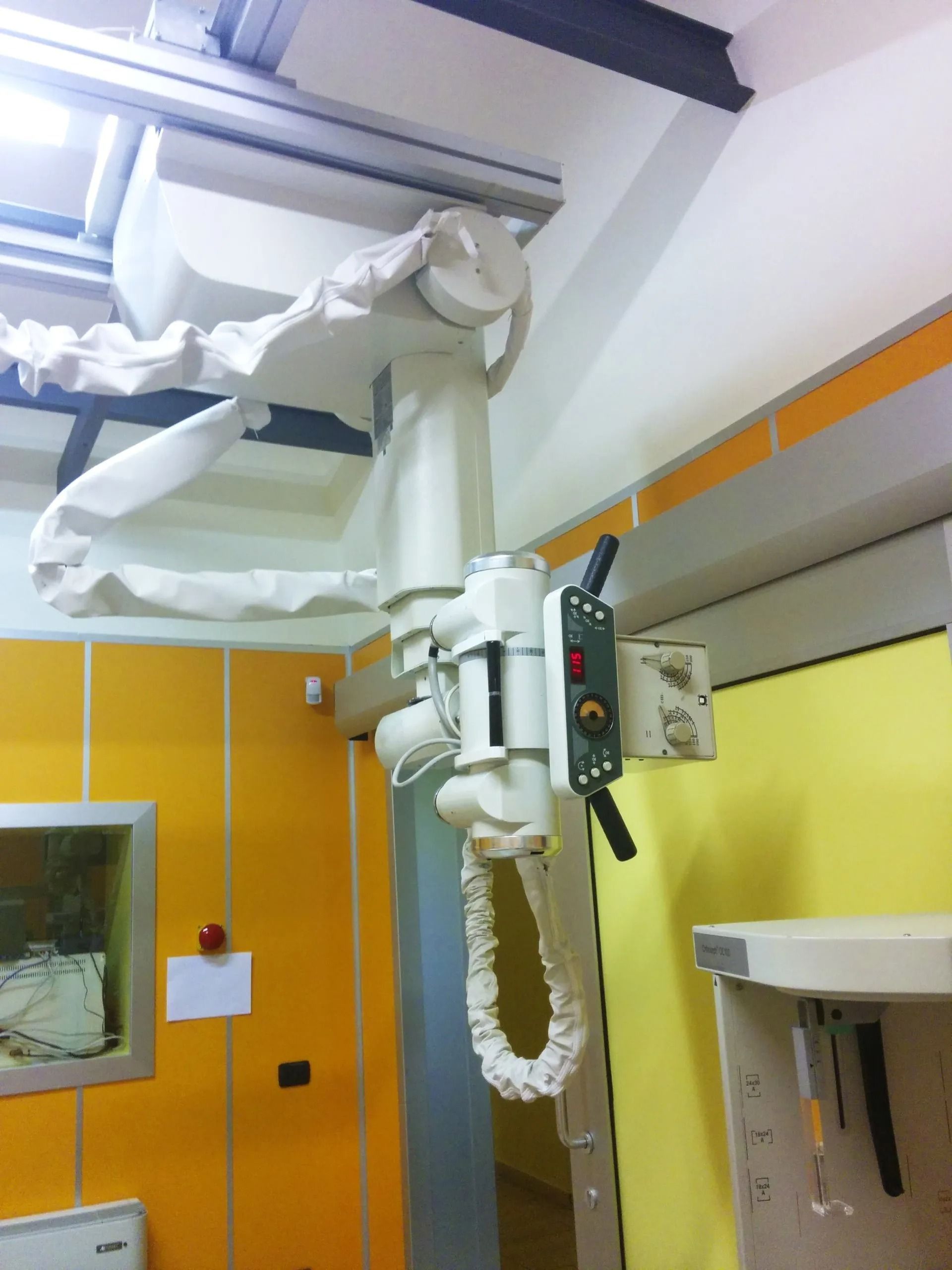 Lampada chirurgica a soffitto e attrezzature ospedaliere in una stanza luminosa con armadietti gialli.