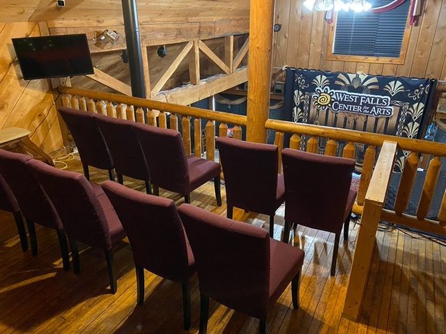 An elevated, interior view of seating in a venue; burgundy chairs face a stage; wood paneling.