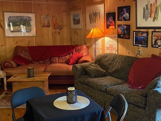 Cozy living room with two sofas, art on wood-paneled walls, small table, lamp, and chairs.