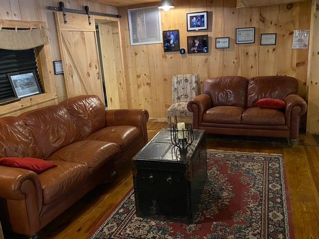 Cozy living room with brown leather sofas, a black coffee table, area rug, and wood-paneled walls.
