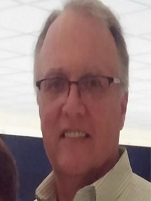 Man wearing glasses and a red patterned tie, smiling in a suit jacket.