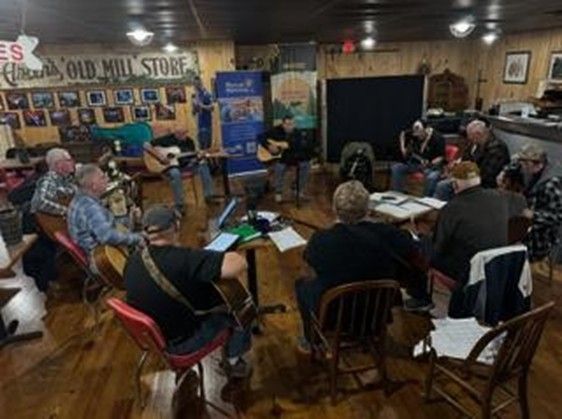 Small music gathering in a cozy room, with seated audience and musicians performing near a bannered stage.
