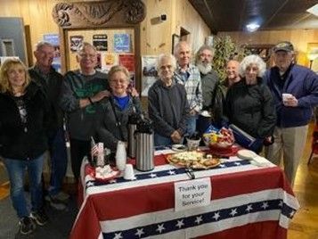 Group gathered around a flag-draped table with cake and snacks at a thank-you celebration