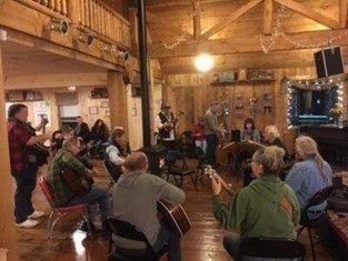People seated in a rustic wooden hall listening to a live acoustic music performance.