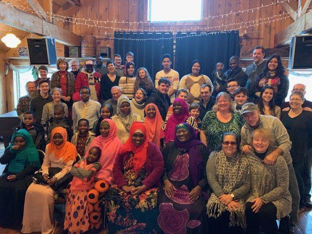 Group of people smiling, posing for a photo in a wooden-paneled building. Some wear colorful headscarves.