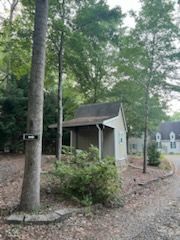 Small shed-like utility building beside a wooded gravel path, surrounded by trees and shrubs.