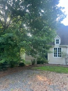 Tree-shaded house with white siding and a gravel driveway in front