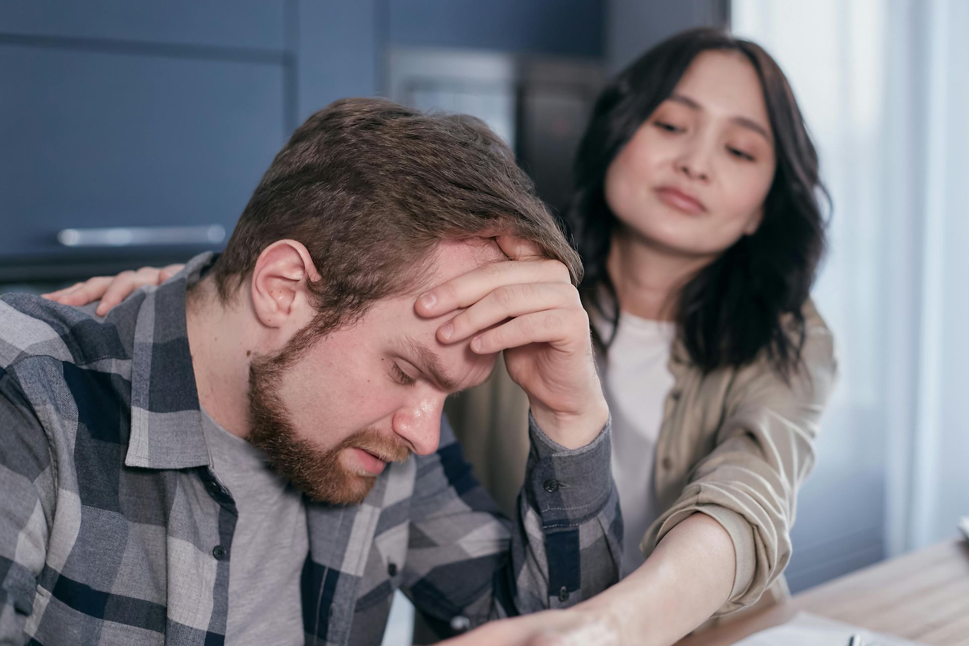 Man holding his head while a woman comforts him at a table with documents โ header for