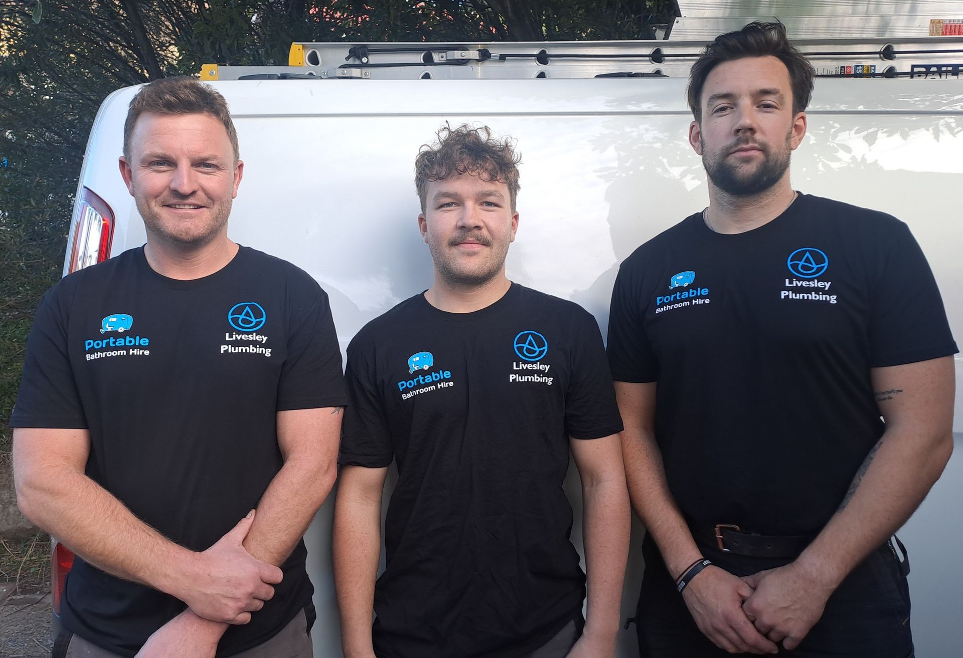 Three men in black shirts are standing in front of a white van.