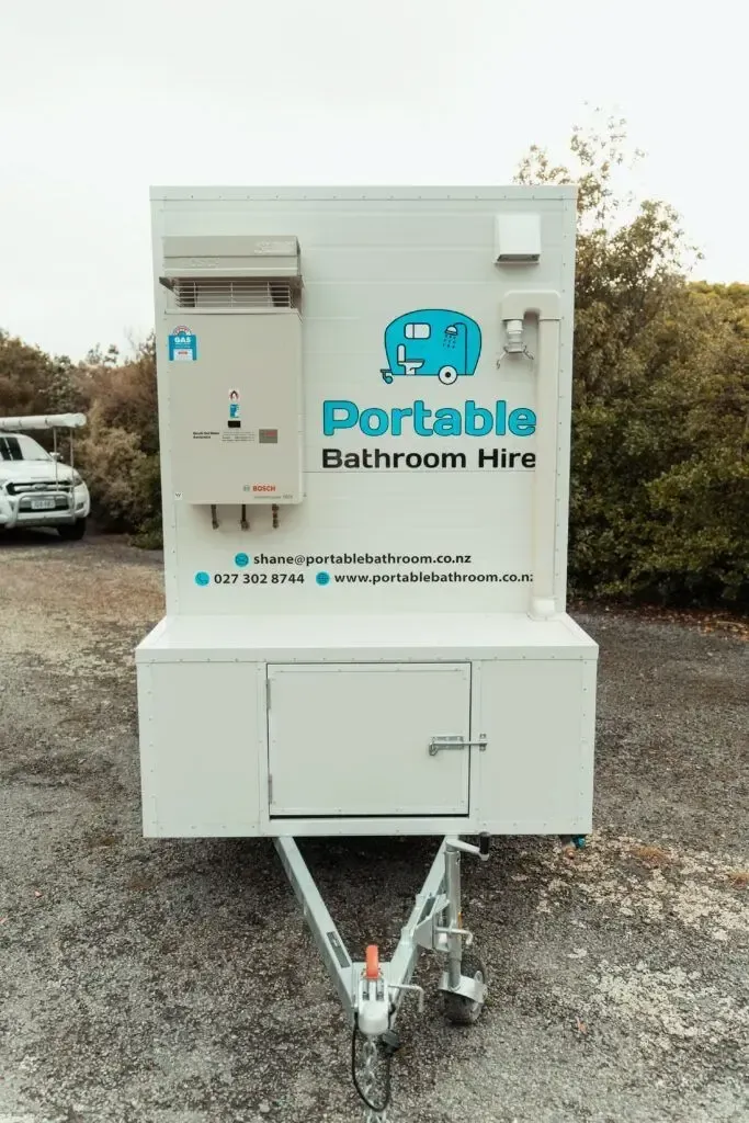A portable bathroom hire trailer is parked in a gravel lot.