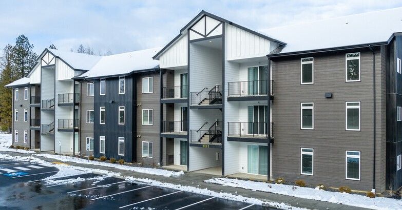 A large apartment building with snow on the roof and a parking lot in front of it.