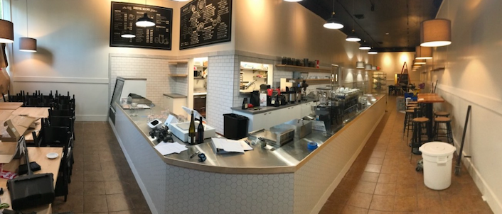 A restaurant with a long counter and tables and chairs.