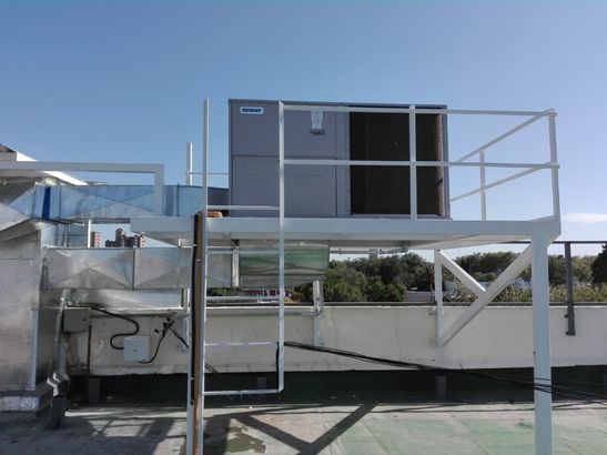 Unidad de climatización industrial en la azotea sobre una plataforma metálica bajo un cielo azul.
