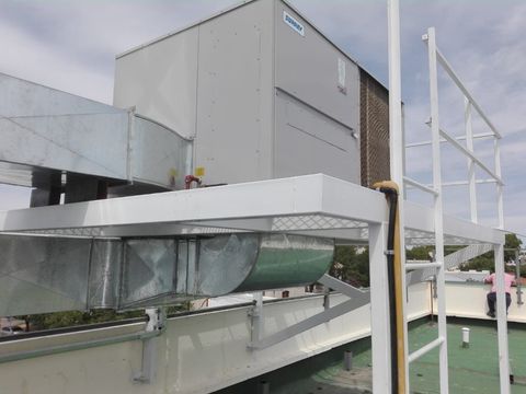 Equipos de climatización y conductos en la azotea junto a un edificio bajo un cielo nublado.