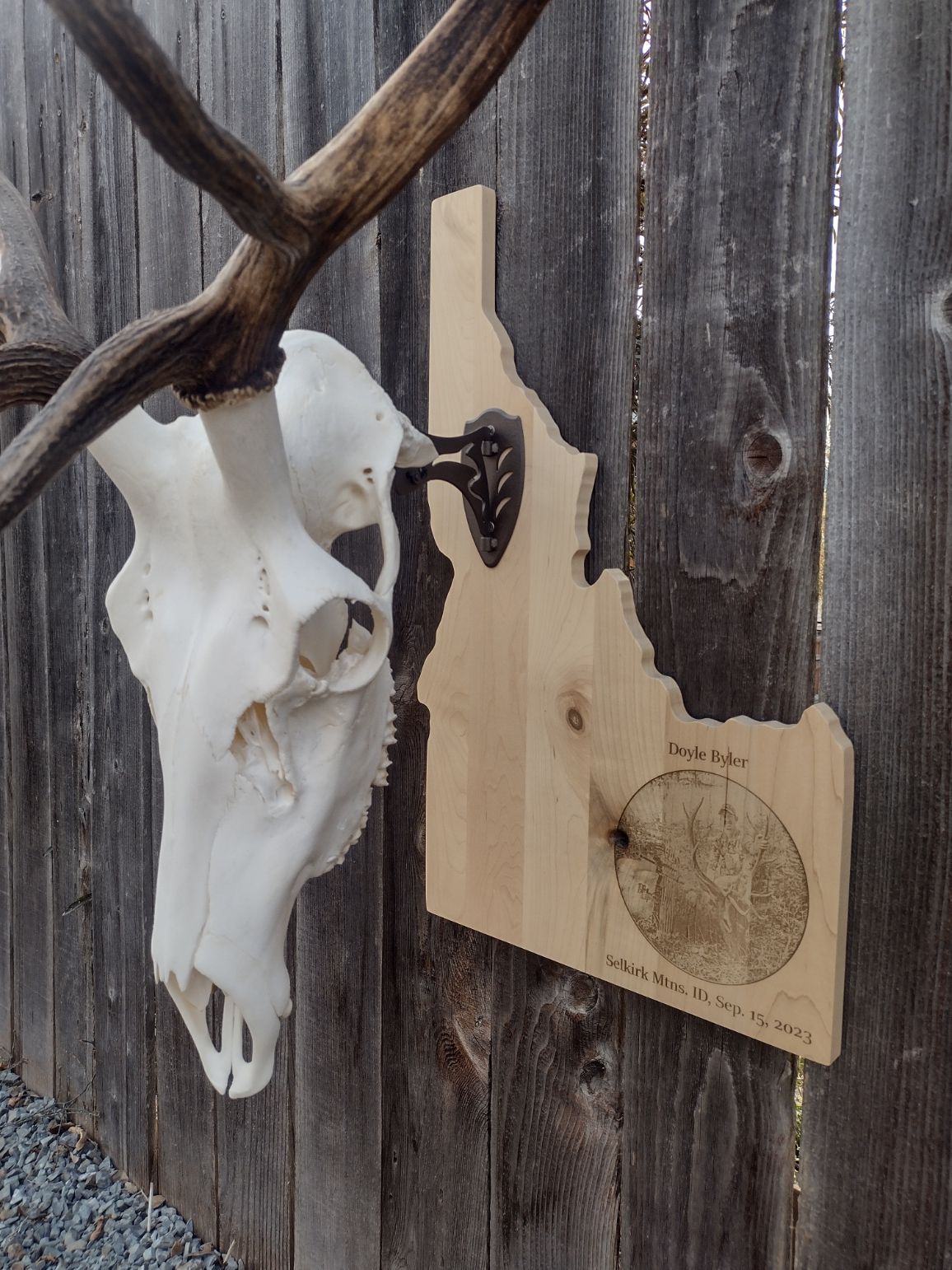 A deer skull is hanging on a wooden fence next to a map of idaho