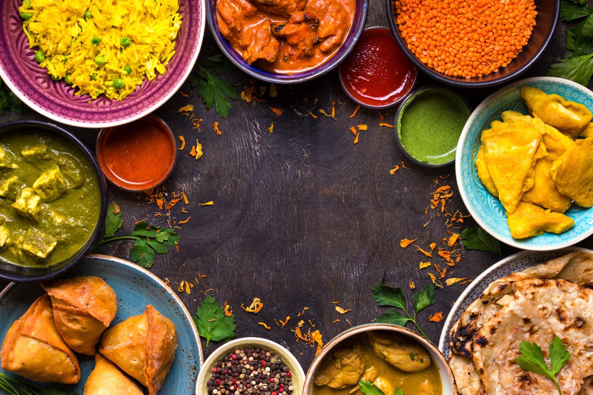 Piatti indiani assortiti, tra cui curry, riso e contorni, disposti in ciotole su uno sfondo scuro.