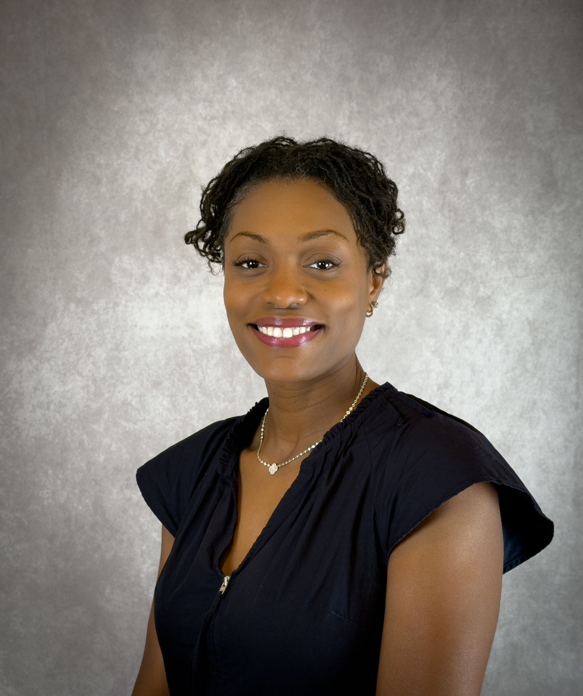 Portrait of a smiling person in a dark navy top against a gray studio backdrop