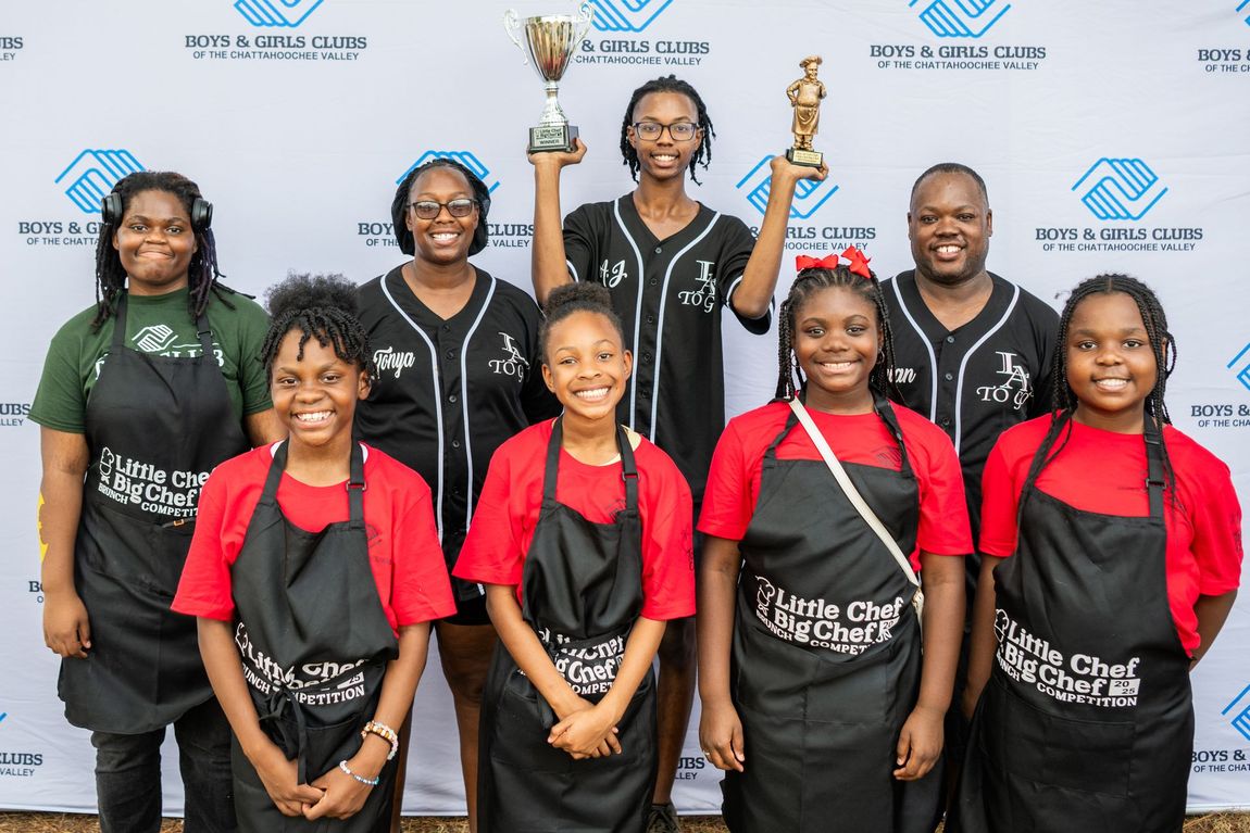 Group of award winners in matching black and red uniforms posing with trophies against a logo backdrop