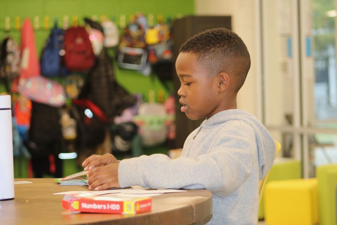 Child sitting at a table with a box of candy, looking toward a store display behind them