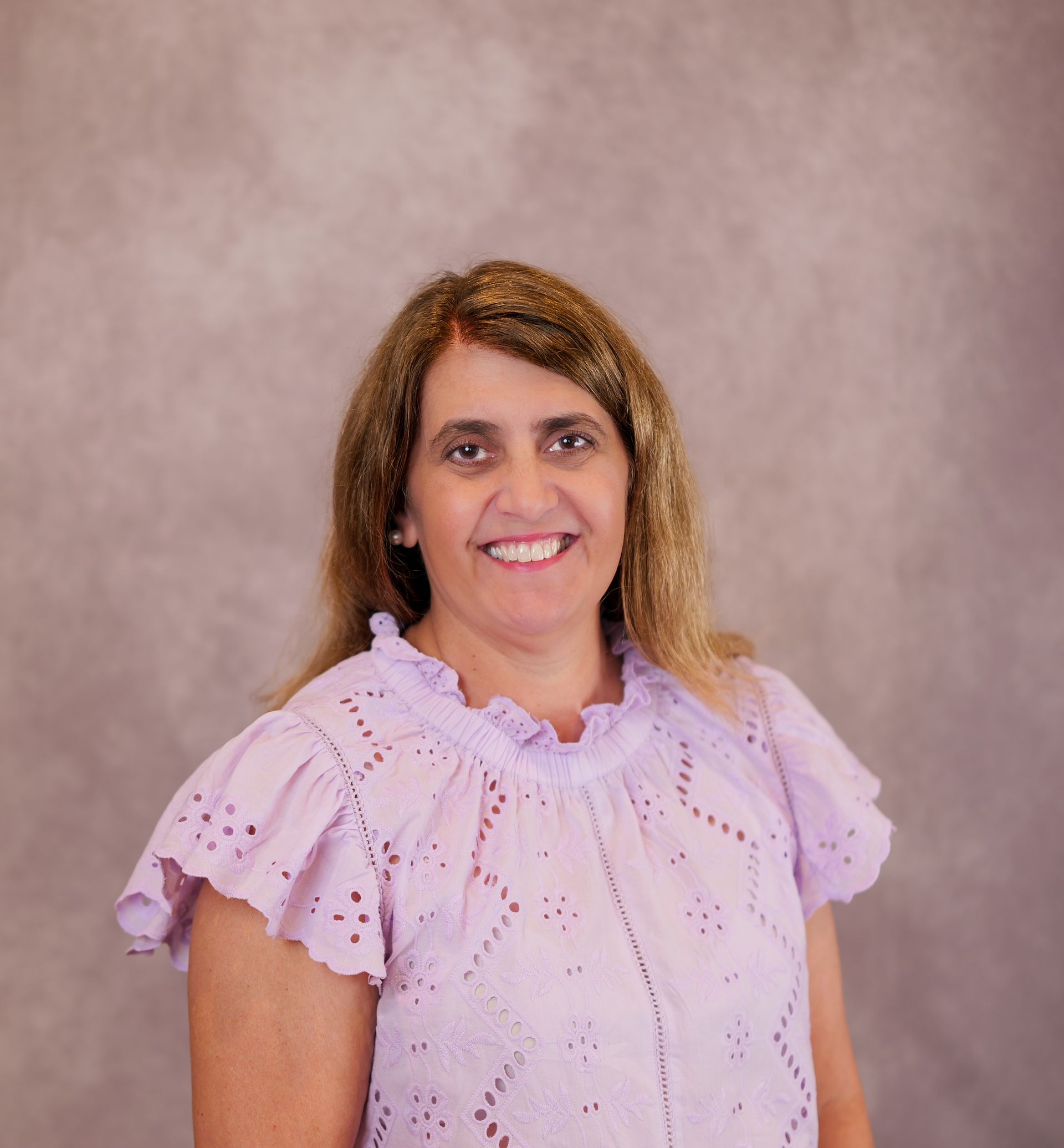 Smiling woman in a white blouse against a gray studio backdrop