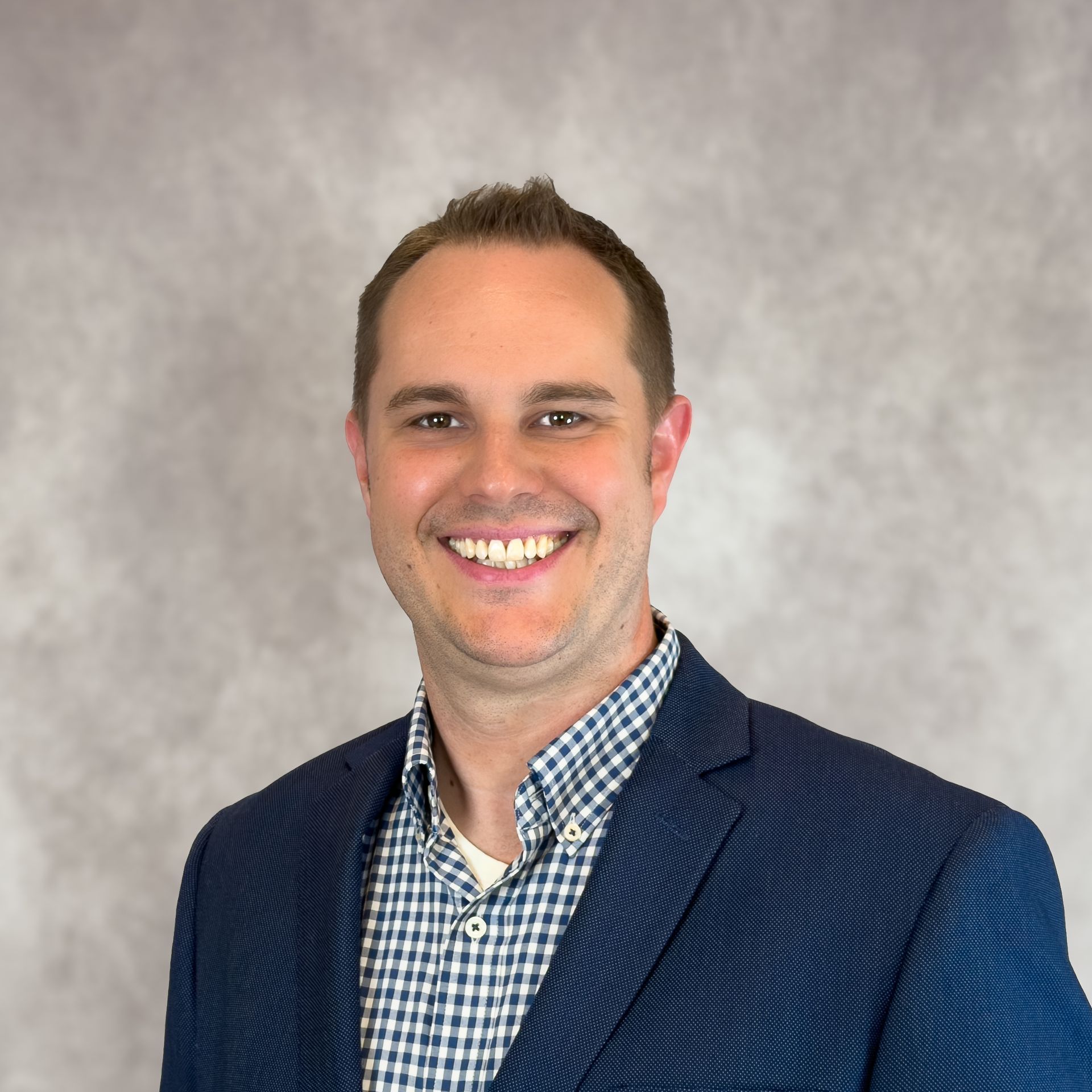 Portrait of a smiling man in a blue blazer and checkered shirt against a gray background
