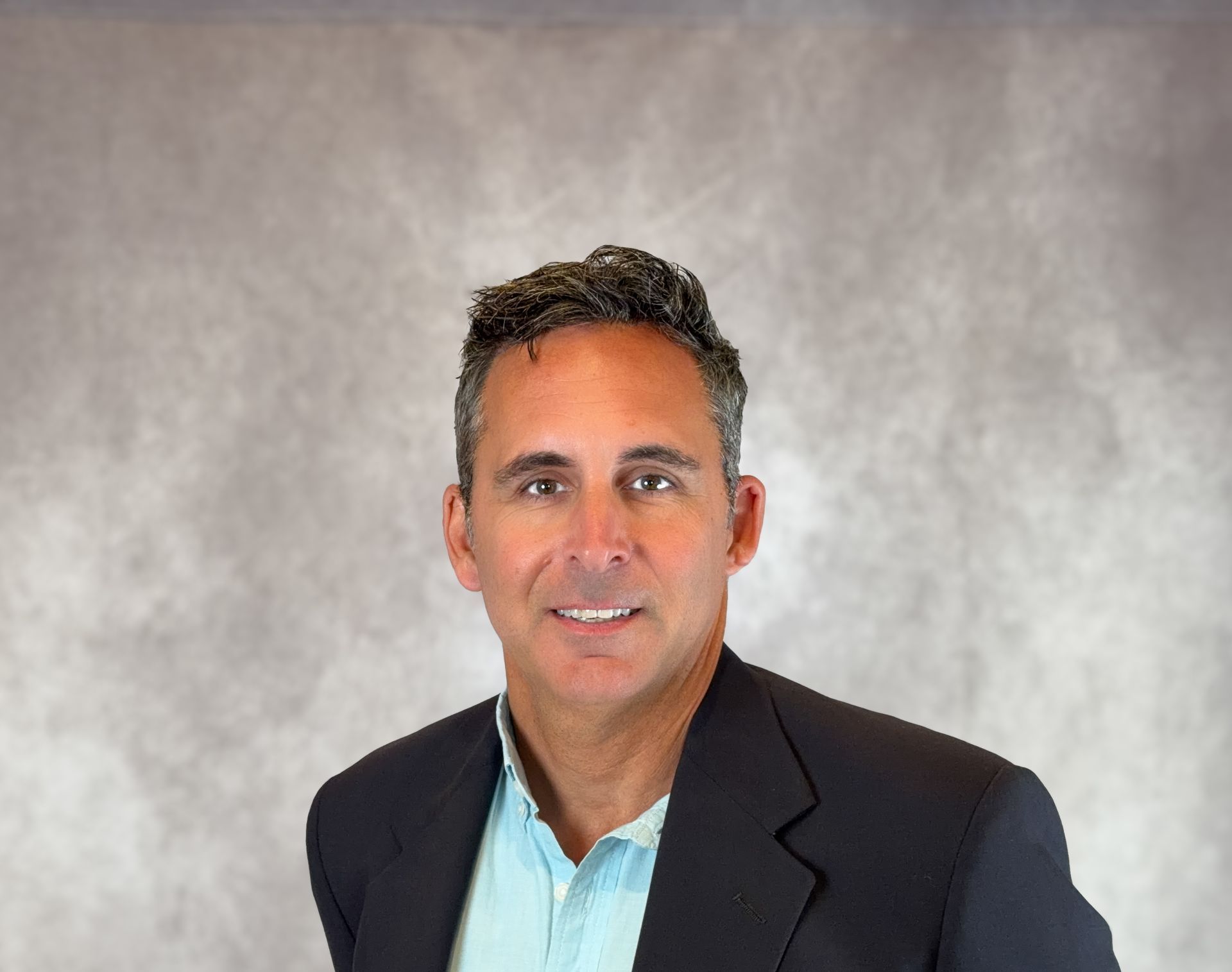 Portrait of a man in a dark blazer and light blue shirt against a gray backdrop