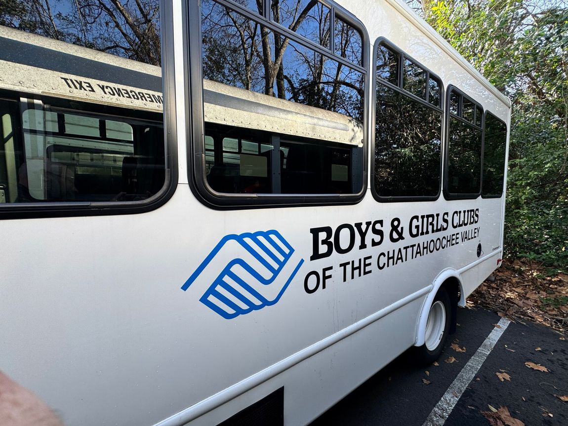 White Boys & Girls Club bus with blue logo parked along a roadside in a wooded area