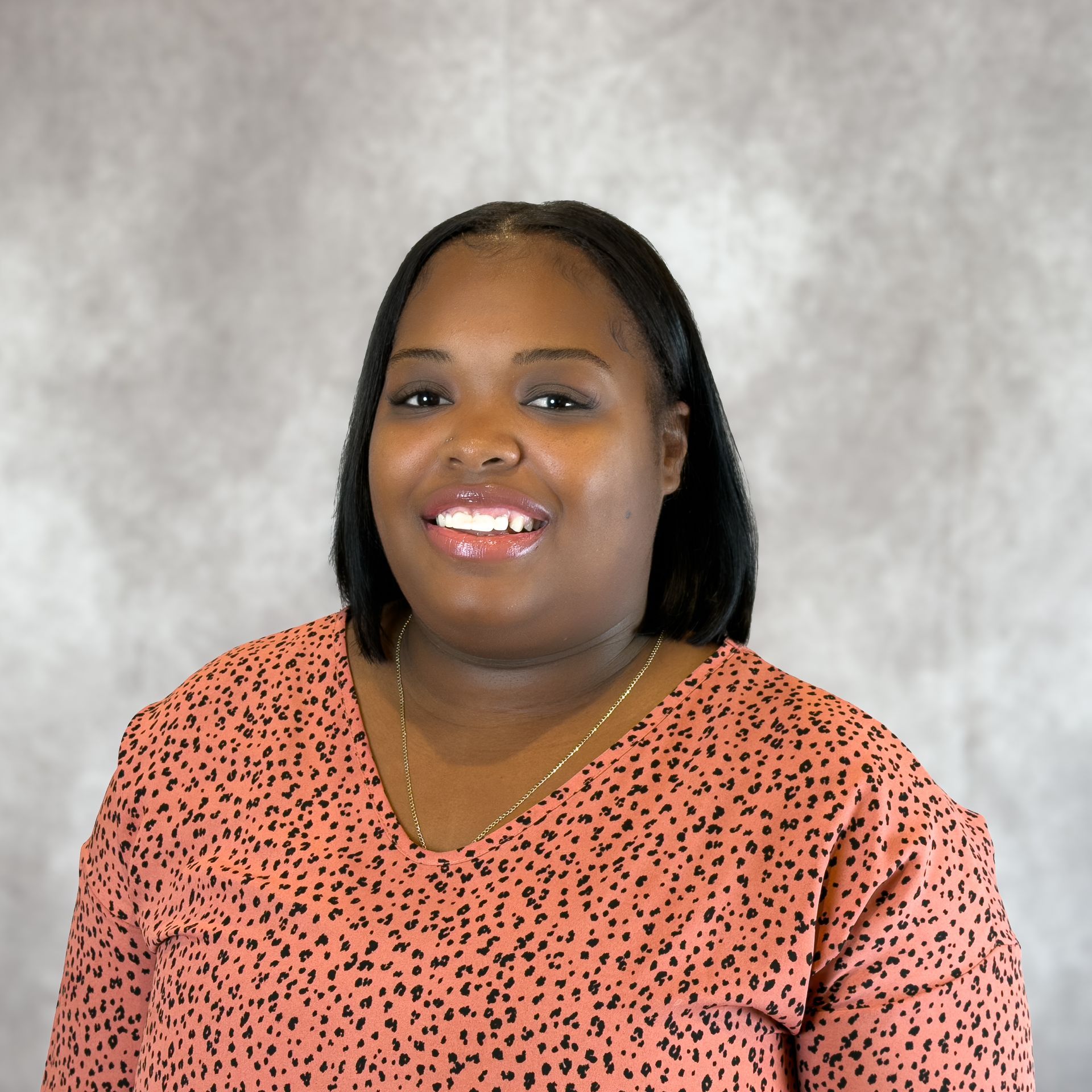 Smiling person in a coral patterned top against a gray backdrop
