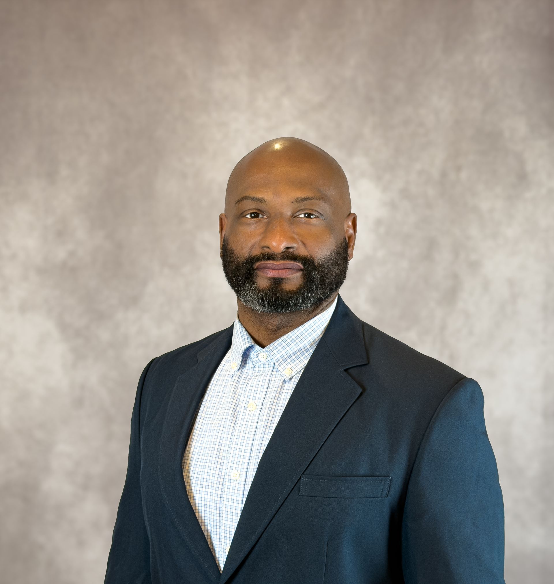 Man in a dark suit and patterned shirt posing against a neutral gray backdrop