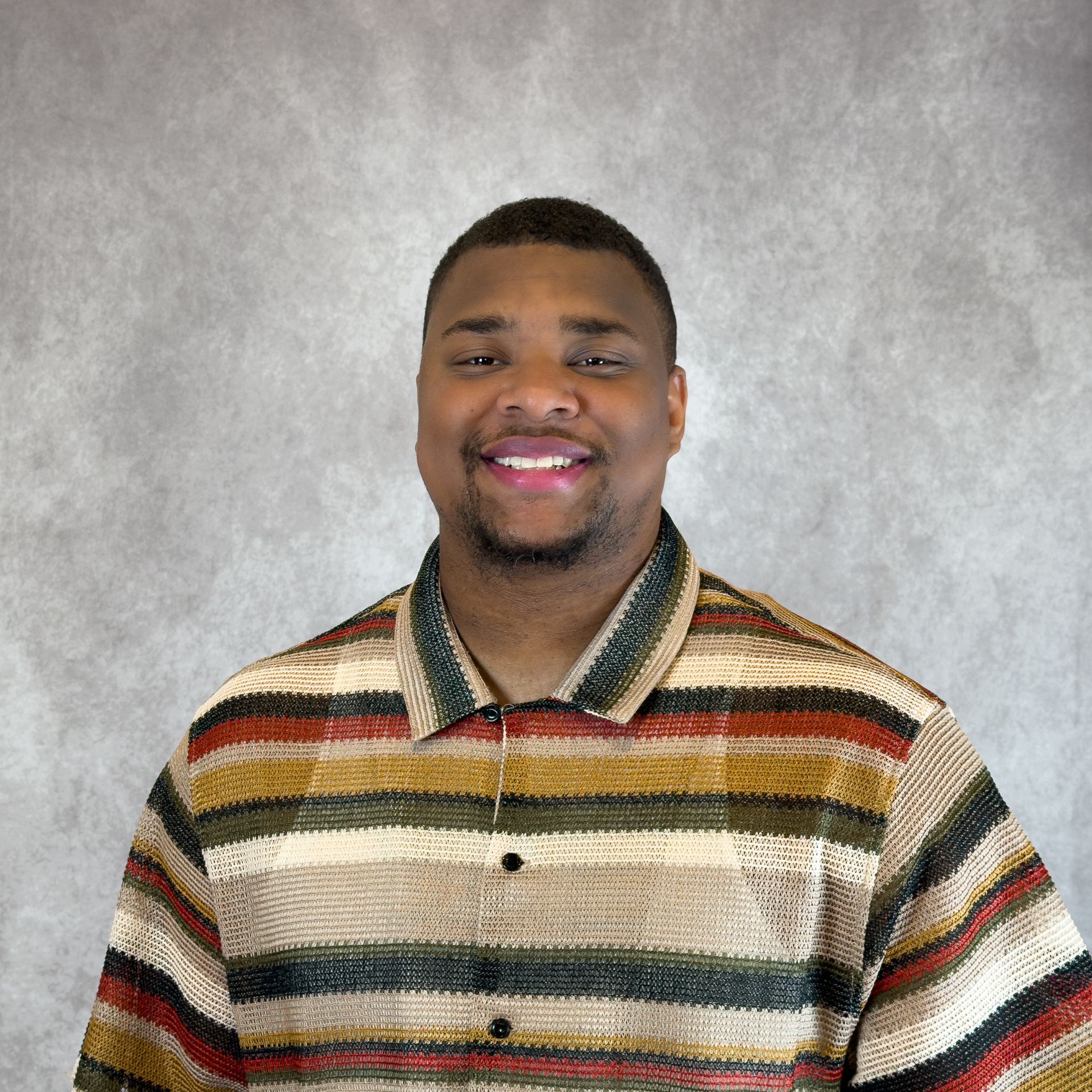 Smiling person in a striped shirt against a gray studio backdrop