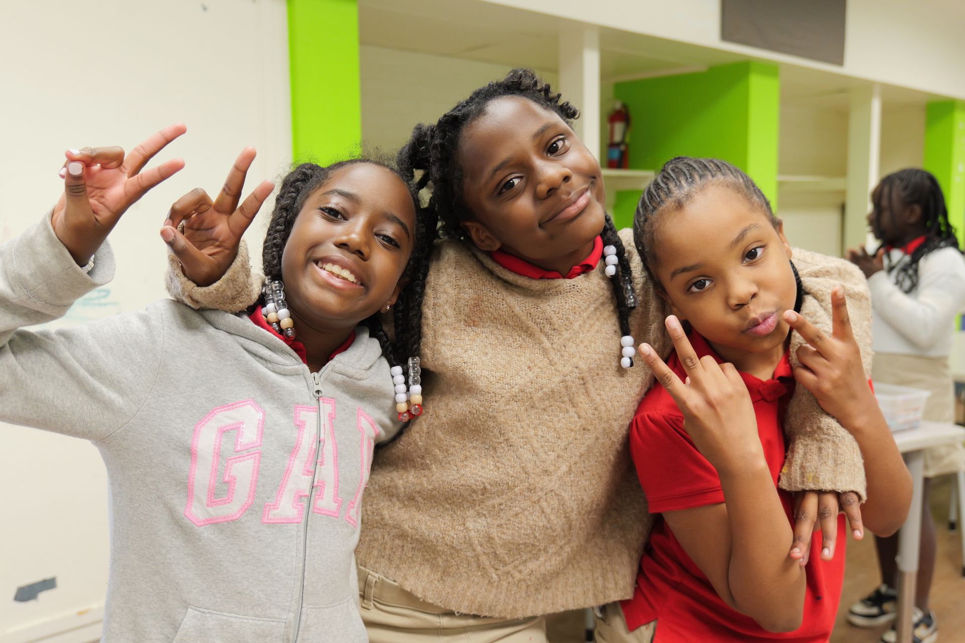 Three smiling people pose indoors, making hand signs in a bright room.