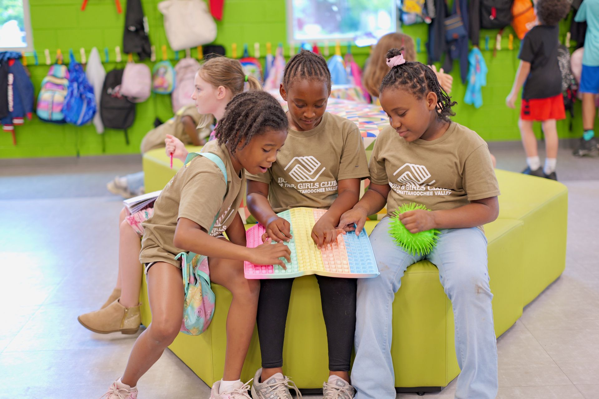 Children sitting on a bench looking at a book together in a colorful classroom.