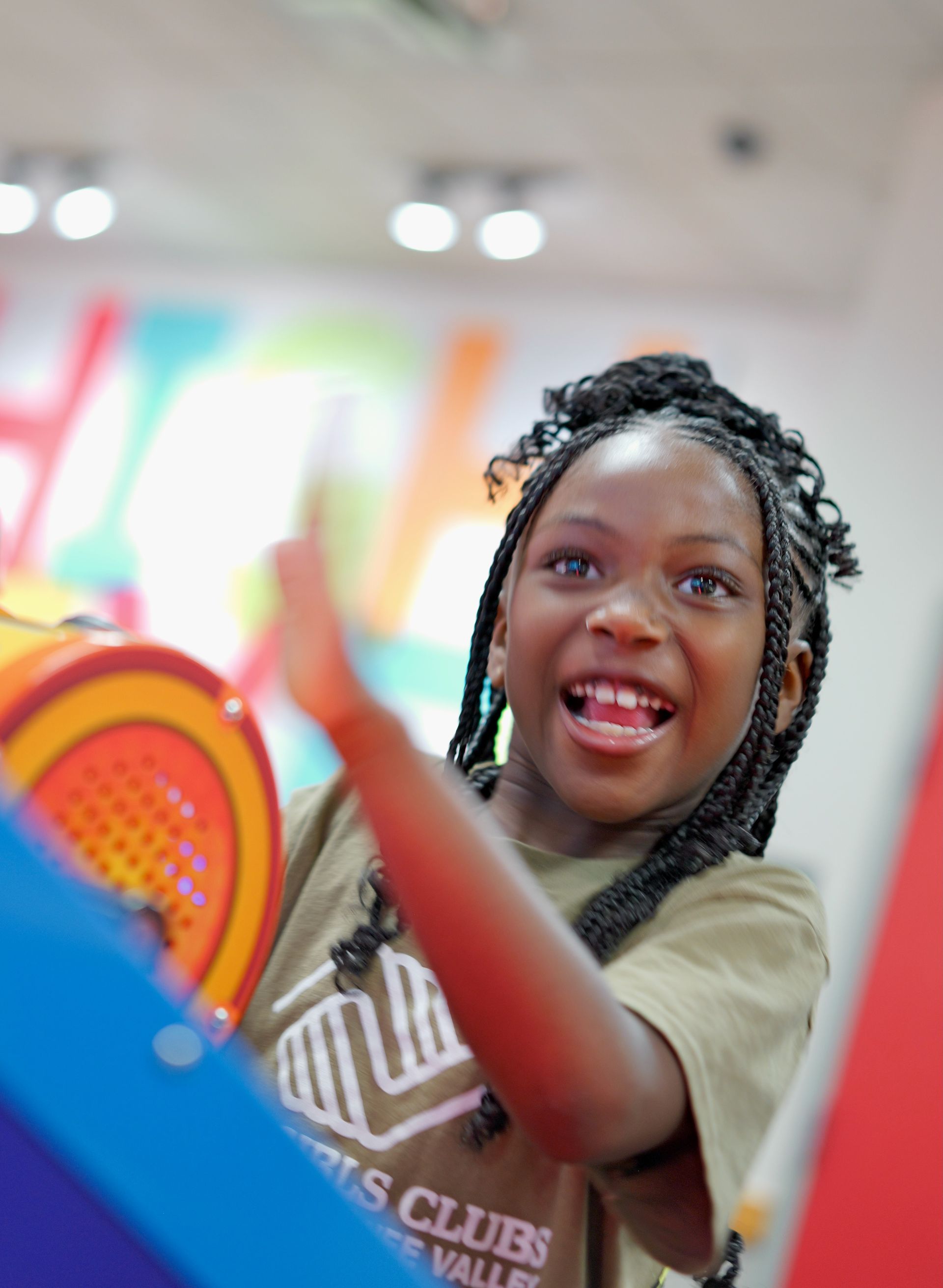 Smiling person reaching out with a colorful paddle in a bright indoor game room