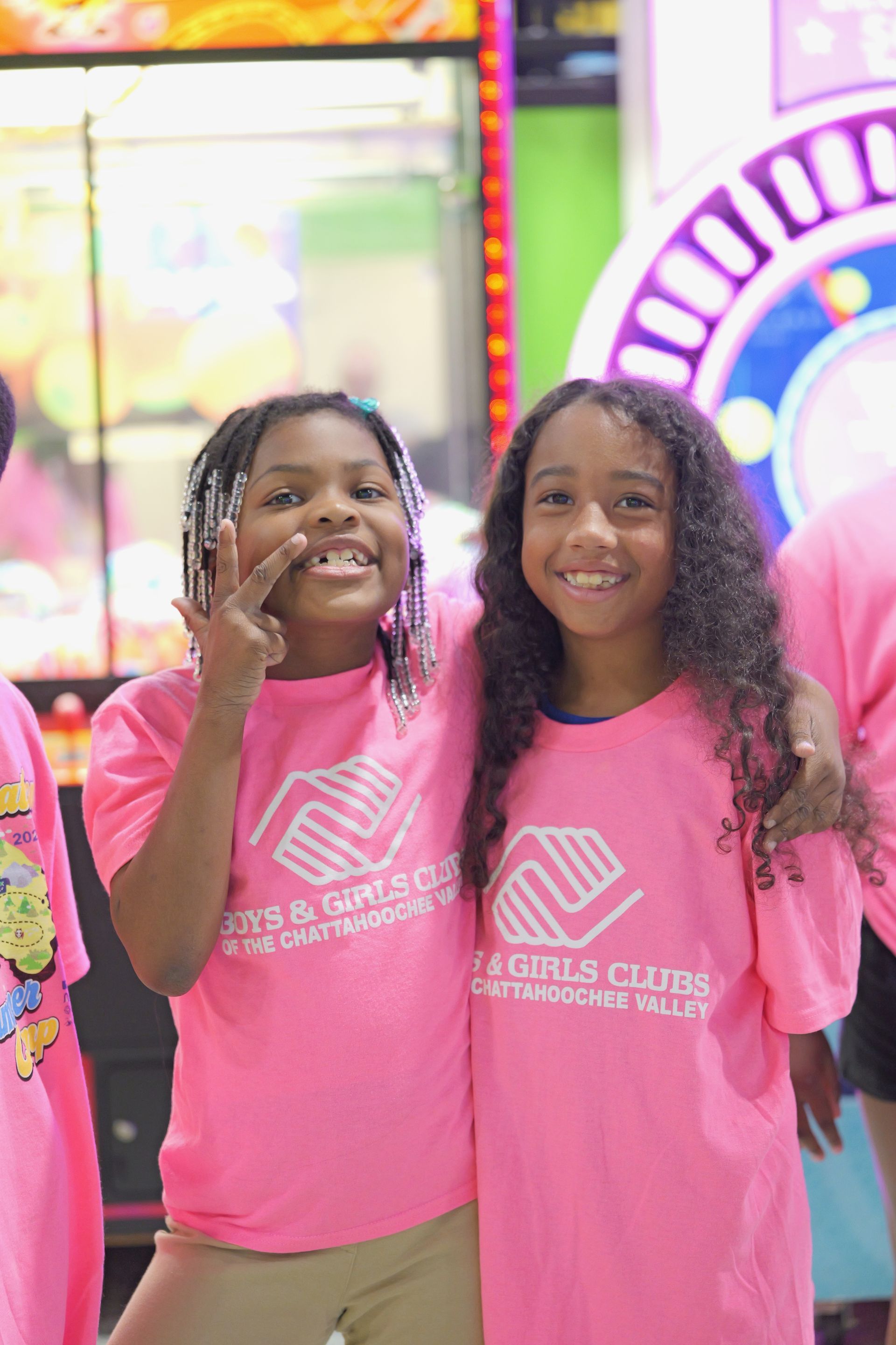 Two children in matching pink shirts smiling and posing in a colorful indoor arcade
