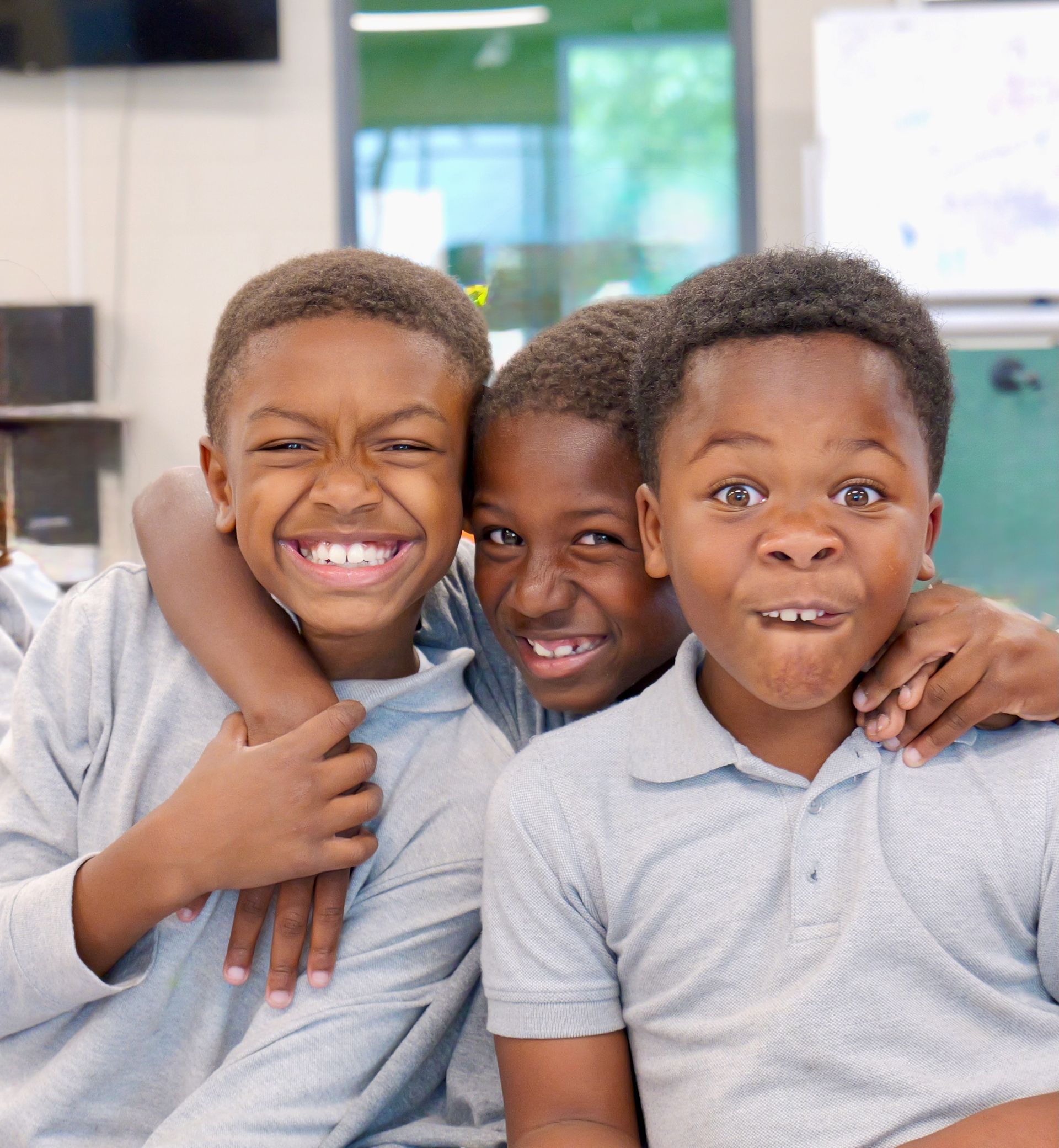 Three smiling children in gray shirts posing closely together indoors