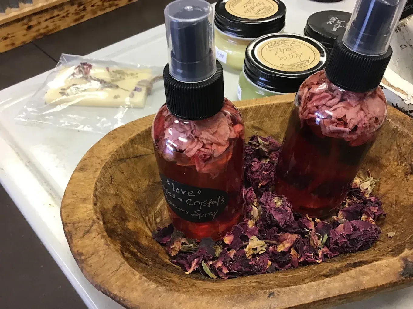 Two pink spray bottles on a wooden tray with dried flower petals and small jars in the background