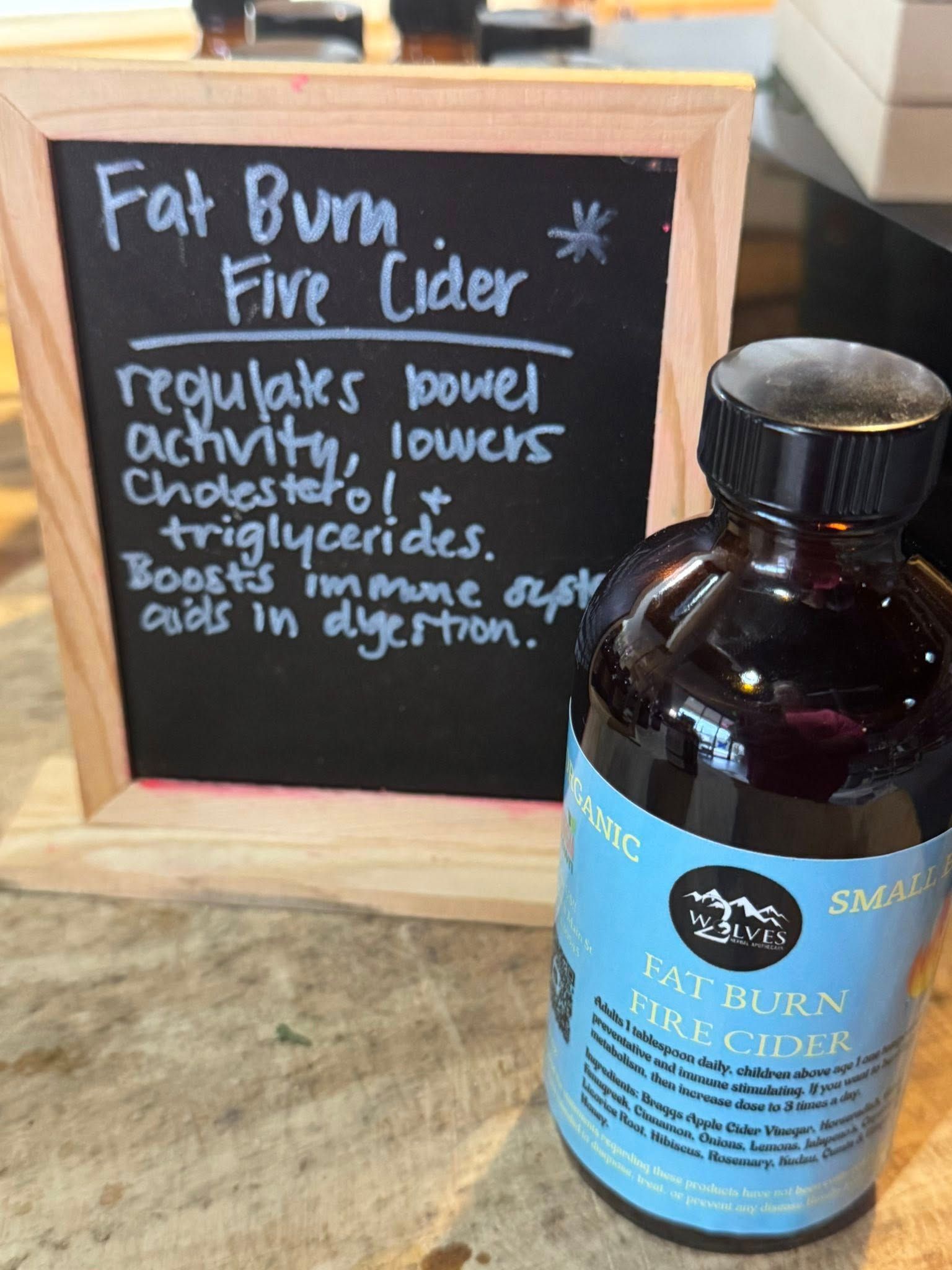 Fat Burn Fire Cider bottle beside chalkboard sign describing digestive and appetite benefits