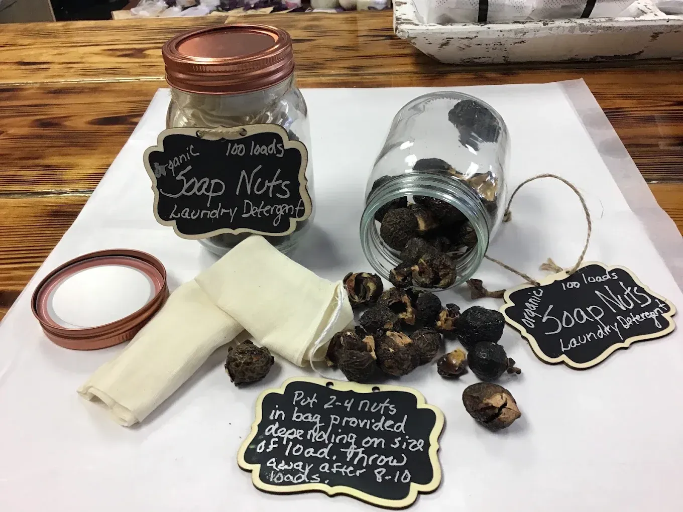 Spilled glass jar of soap nuts with chalkboard signs and a copper lid on a wooden table