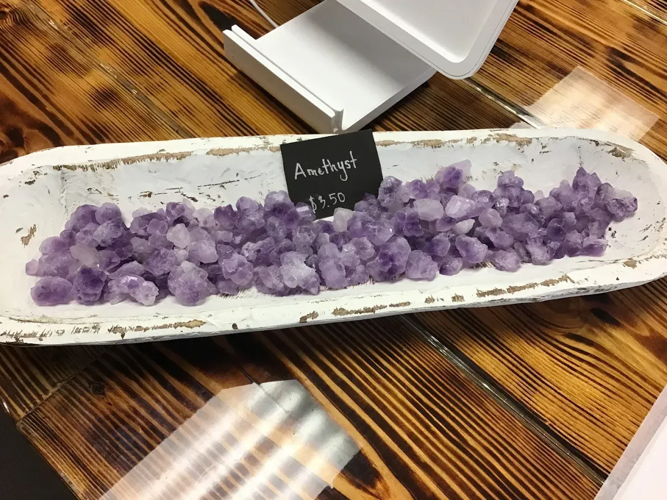 Purple crystals arranged on a long white tray with a small label on a wooden table.