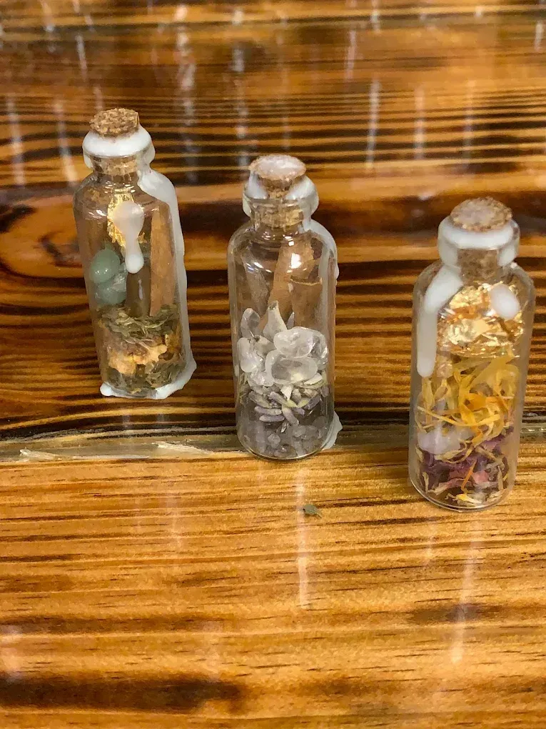 Three small glass bottles with corks, each holding dried plant or insect specimens on a wooden table. Three small glass bottles with corks, each holding dried plant or insect specimens on a wooden table.