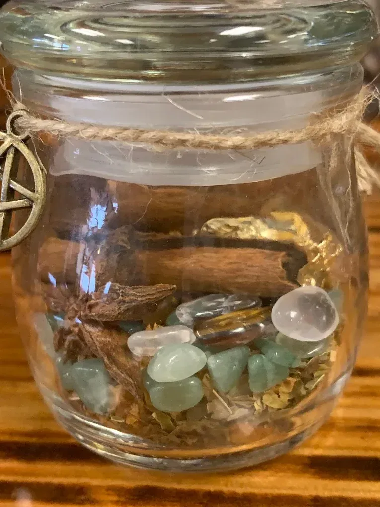 Small glass jar filled with colorful tumbled stones and shells on a wooden surface