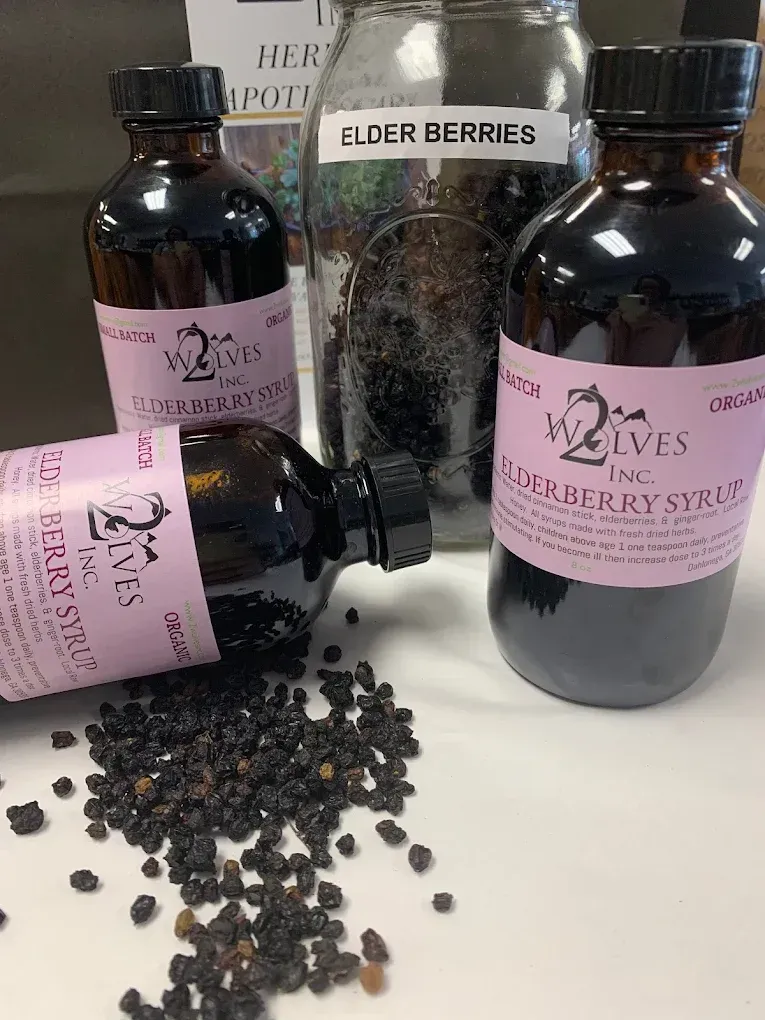 Elderberry syrup bottles and dried elderberries on a table, with one bottle lying on its side.
