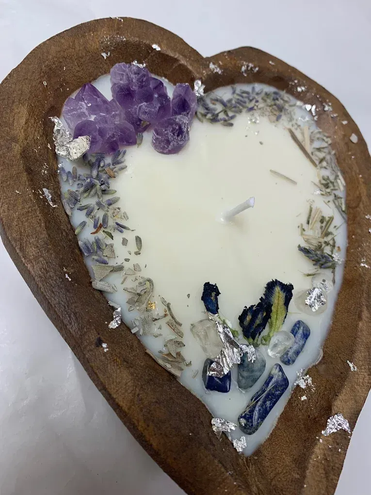 Heart-shaped wooden tray candle with purple crystals and dried herbs around white wax