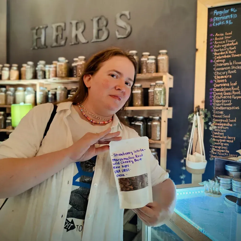 Person holding a bag of herbs inside a shop with shelves of jars and a large HERBS sign.