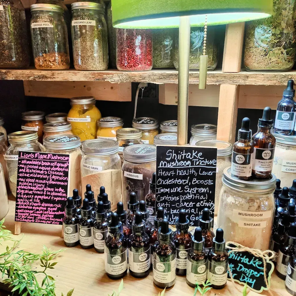 A shop shelf with jars, bottles, and handwritten signs for herbs, tinctures, and natural remedies.