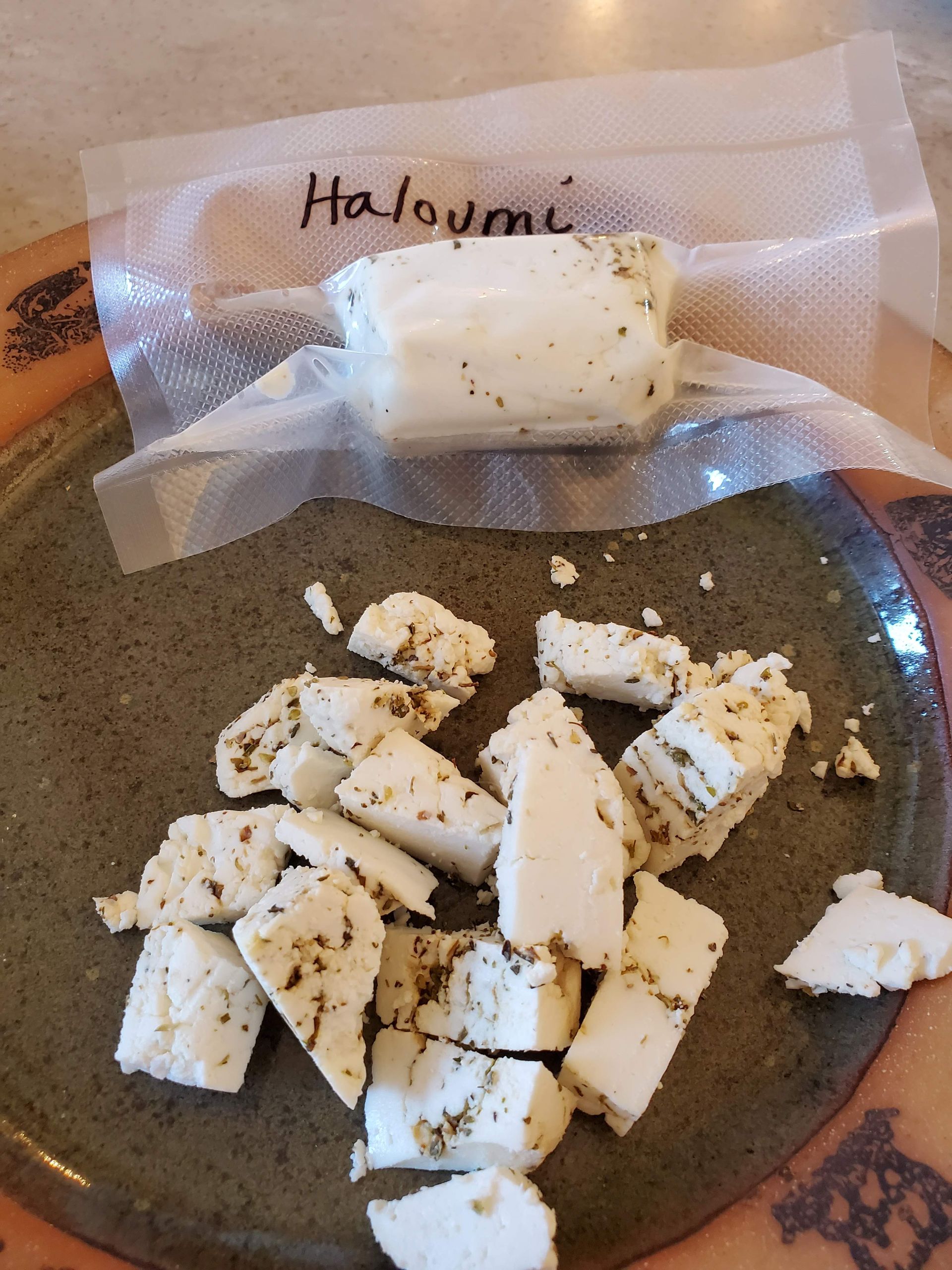 Haloumi cheese in a bag, and chopped pieces on a plate. The cheese is white with herbs.