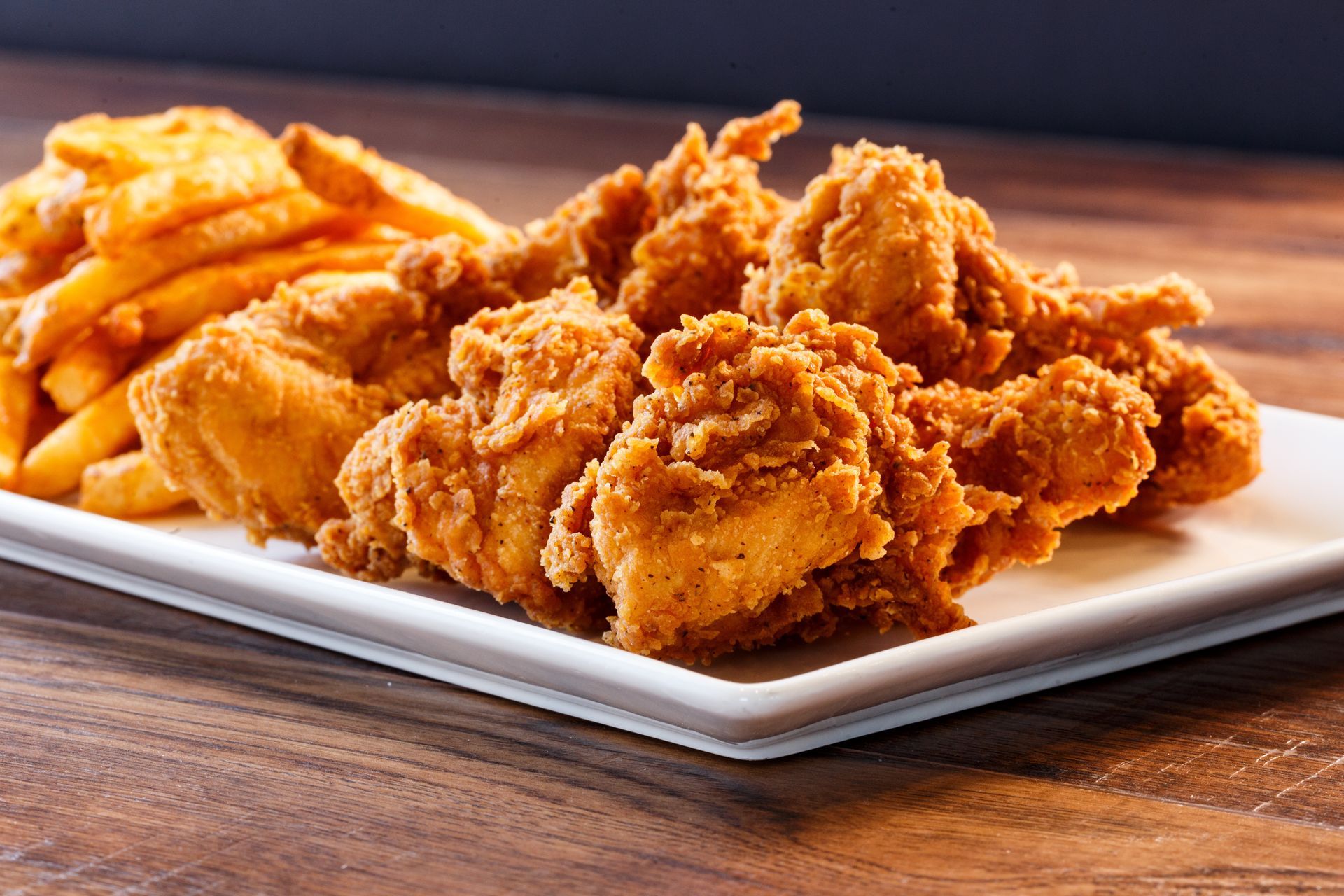 Fried chicken tenders and fries on a white rectangular plate.