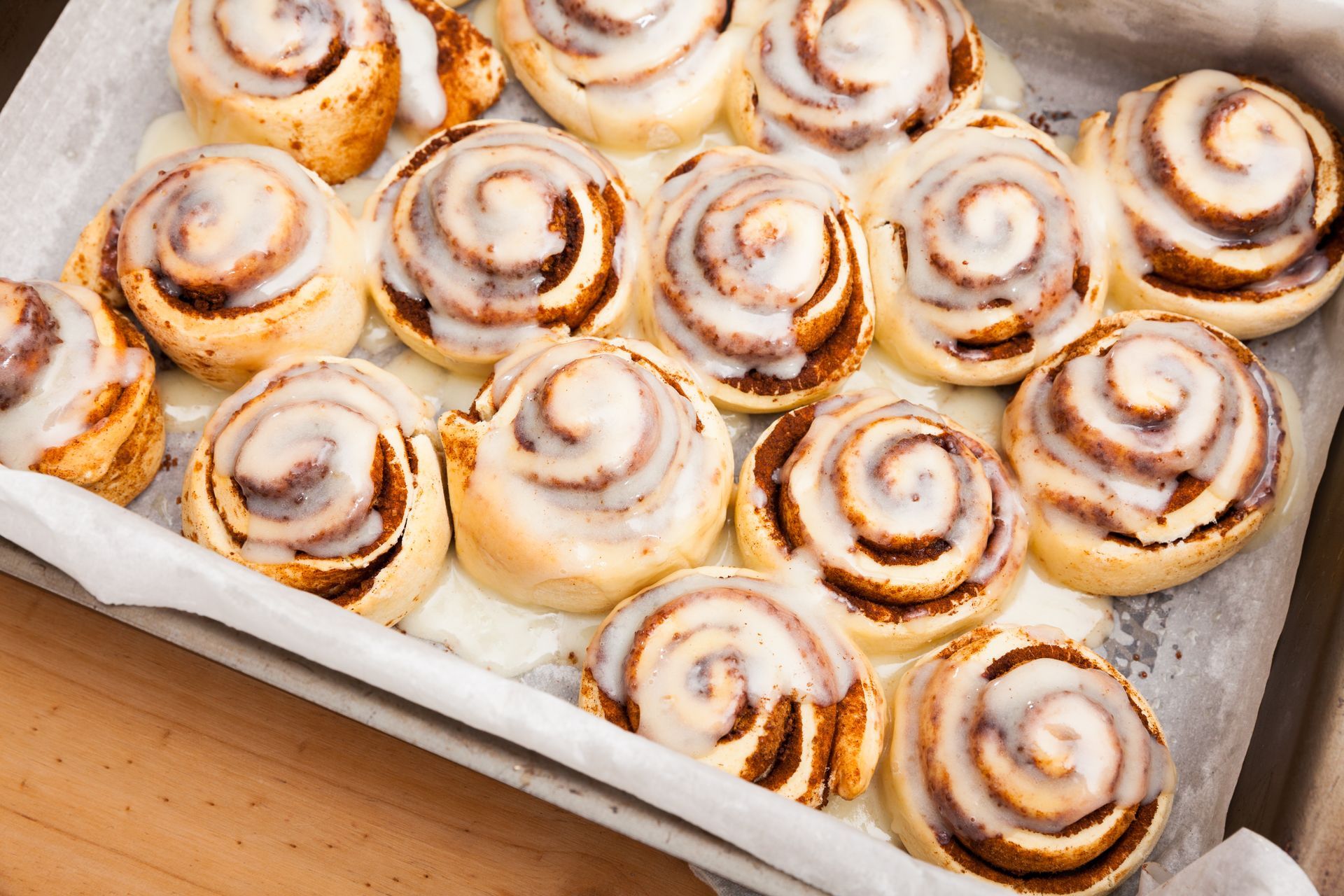 Cinnamon rolls in a baking pan, topped with white icing, sitting on parchment paper.